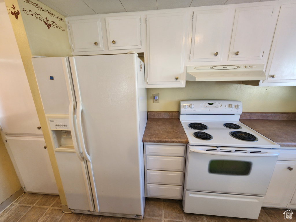 Kitchen with under cabinet range hood, white appliances, dark countertops, and white cabinets
