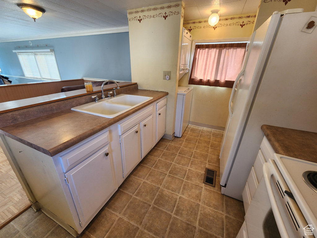 Kitchen featuring a peninsula, a sink, dark countertops, white cabinets, and white appliances