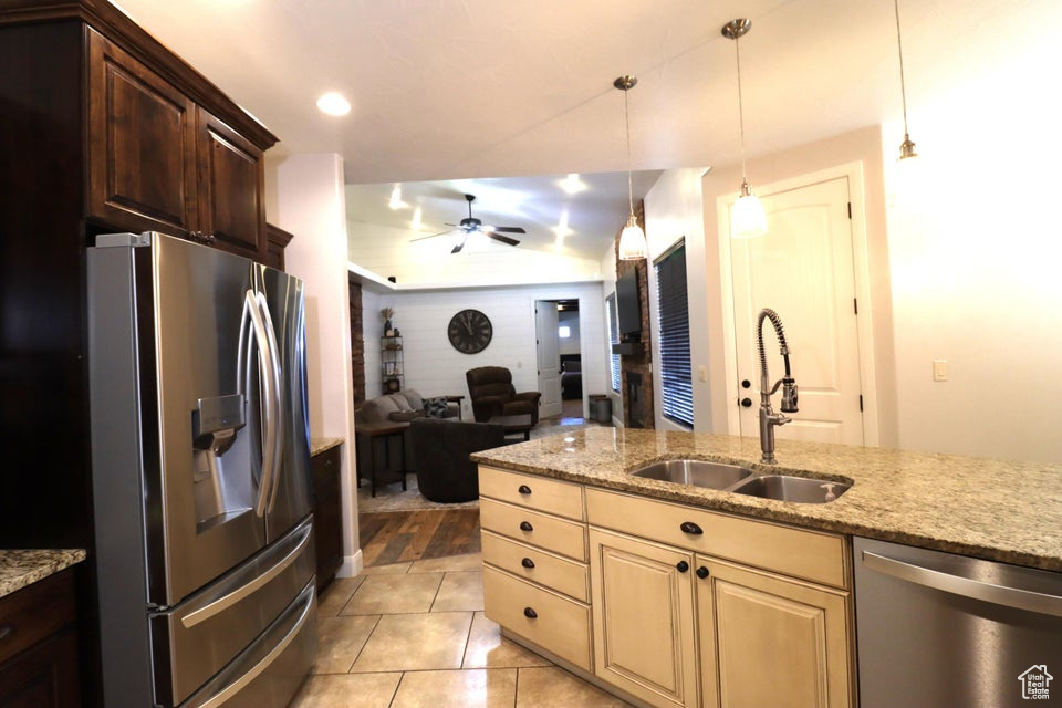 Kitchen featuring a sink, stainless steel appliances, ceiling fan, open floor plan, and light stone countertops