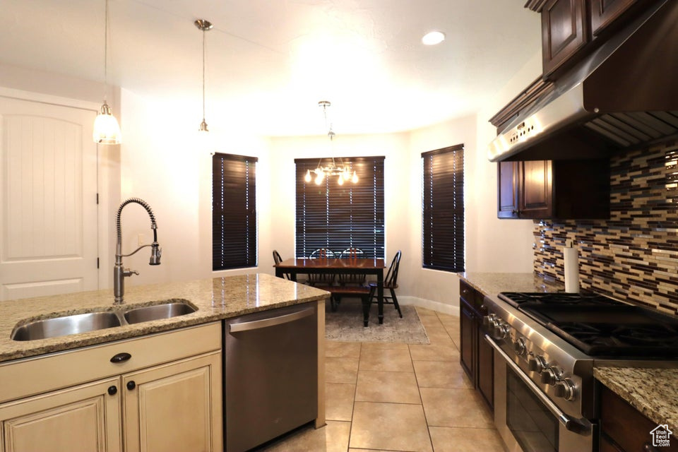 Kitchen featuring light stone countertops, under cabinet range hood, a sink, decorative backsplash, and appliances with stainless steel finishes