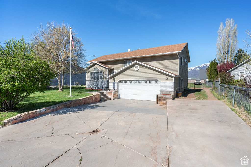 View of front of house with driveway, a mountain view, fence, a garage, and a front lawn