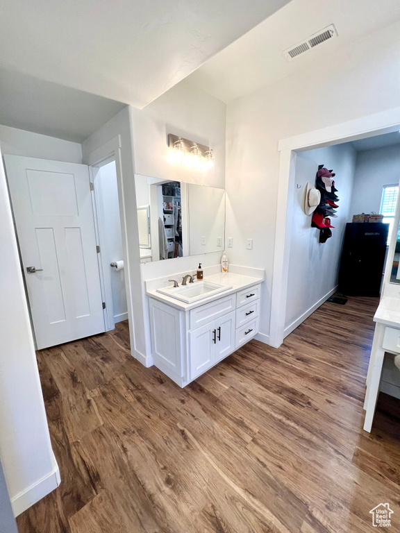 Bathroom featuring wood finished floors, vanity, visible vents, a walk in closet, and baseboards
