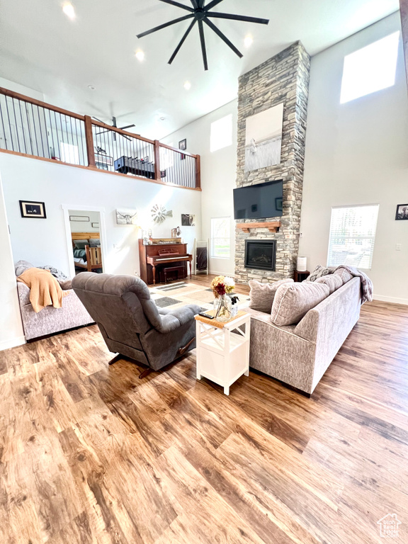 Living area with a ceiling fan, a stone fireplace, high vaulted ceiling, and wood finished floors