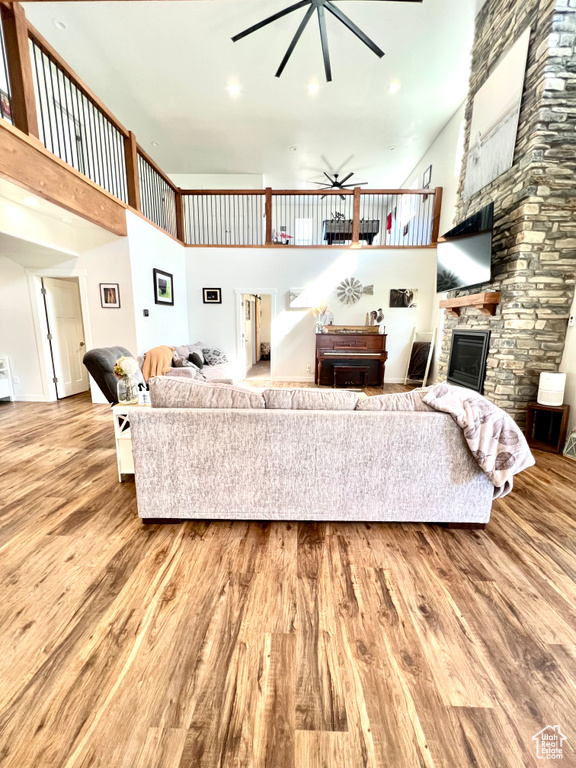 Living room with a high ceiling, wood finished floors, a fireplace, and ceiling fan