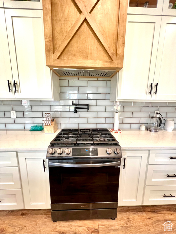 Kitchen featuring backsplash, stainless steel gas range oven, light wood finished floors, and white cabinets