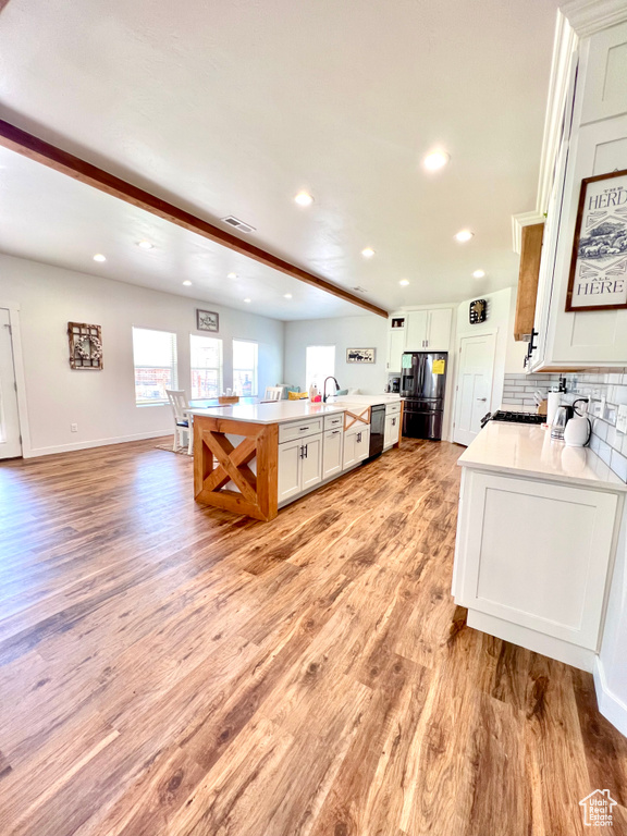 Kitchen with light wood-type flooring, dishwasher, light countertops, open floor plan, and stainless steel fridge with ice dispenser