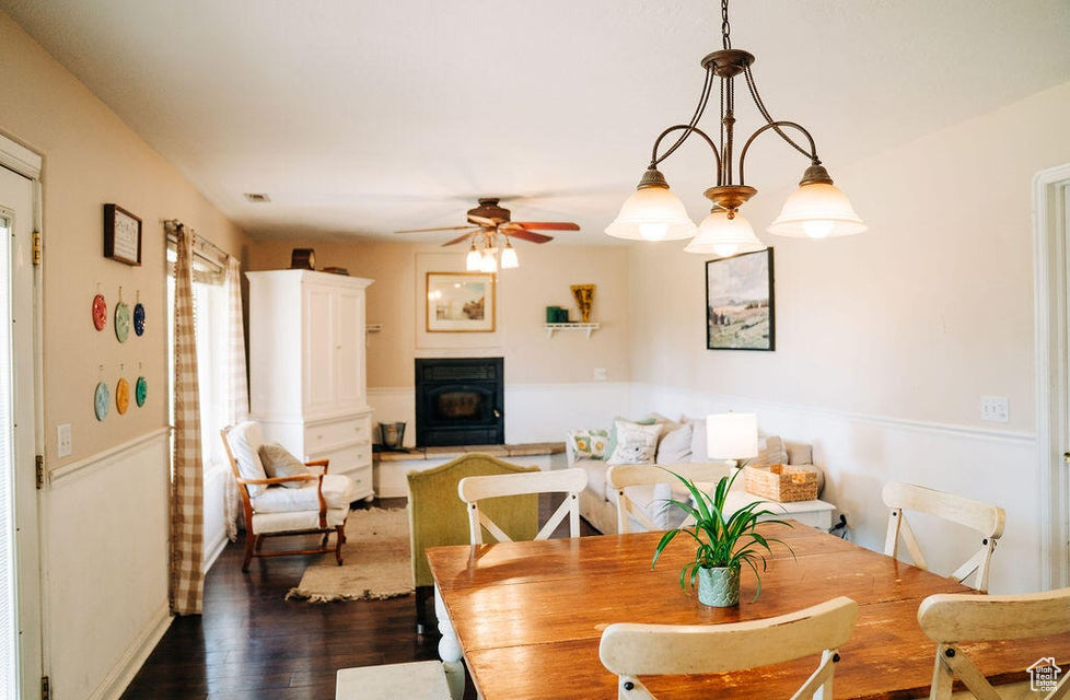Dining area with a ceiling fan, dark wood-style flooring, a wood stove, and baseboards