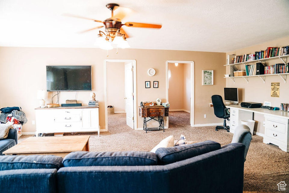 Carpeted living room featuring built in desk, baseboards, and a ceiling fan