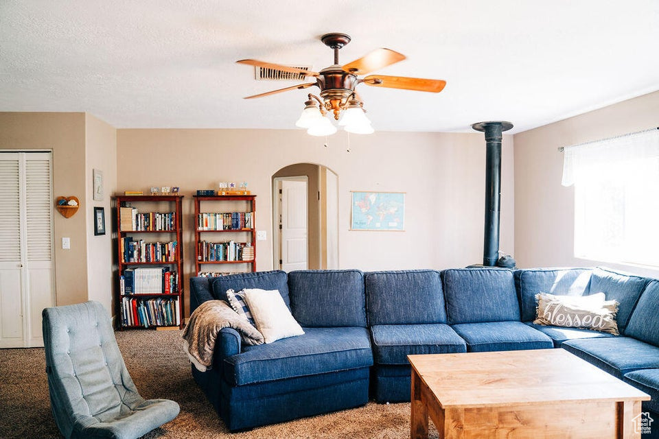 Living area with light colored carpet, arched walkways, a ceiling fan, and visible vents