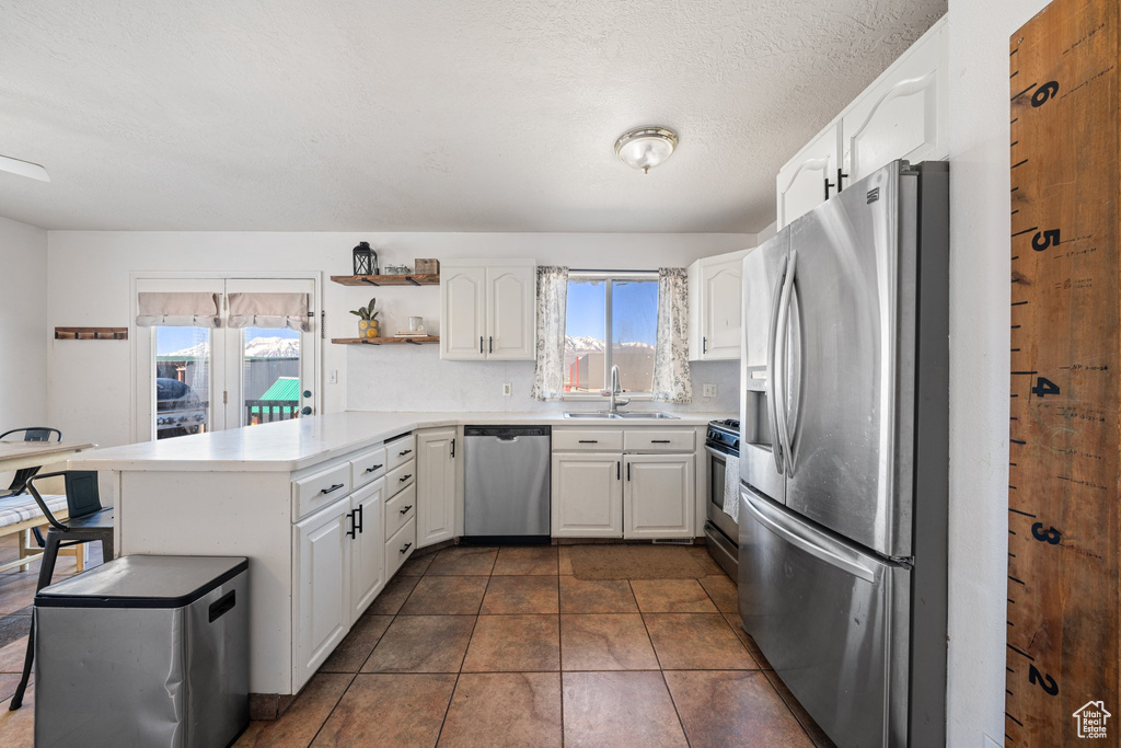 Kitchen featuring a sink, white cabinetry, open shelves, a peninsula, and appliances with stainless steel finishes