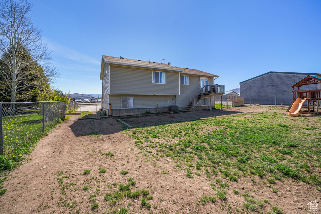 Back of house featuring cooling unit, a playground, a fenced backyard, a yard, and stairs
