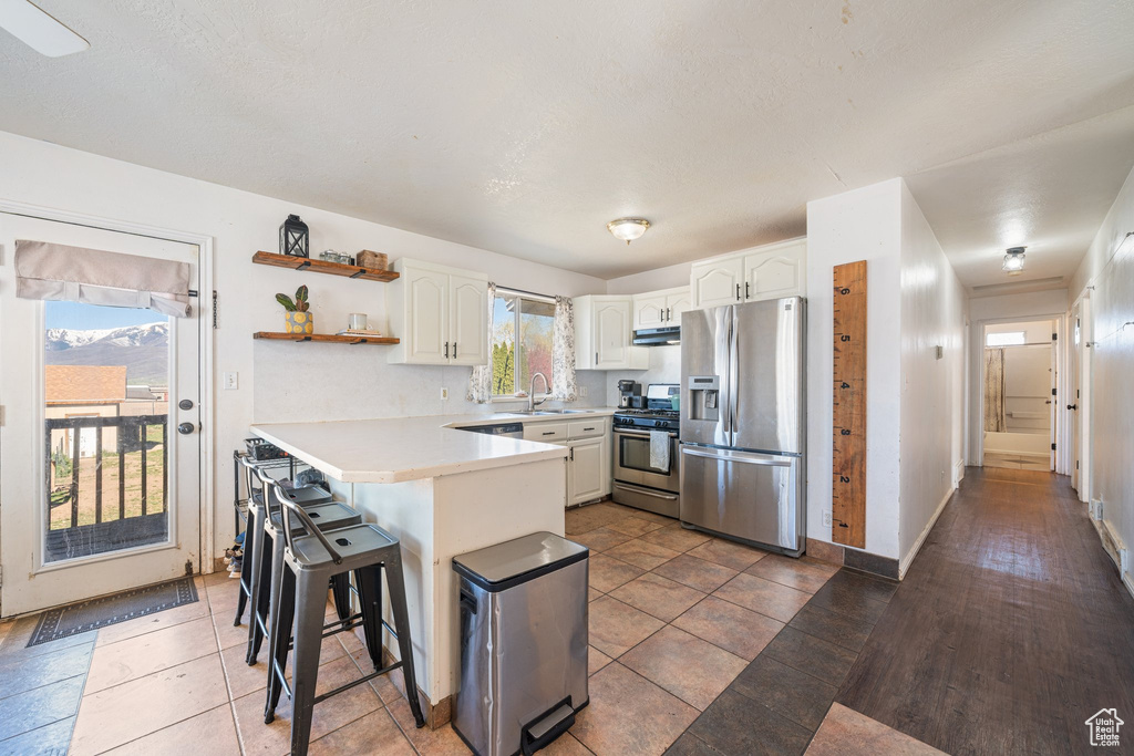 Kitchen featuring a peninsula, a sink, open shelves, stainless steel appliances, and white cabinetry