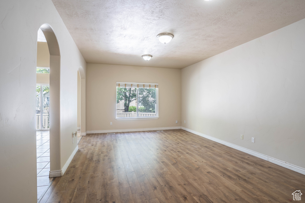 Unfurnished room featuring arched walkways, baseboards, a textured ceiling, and wood finished floors