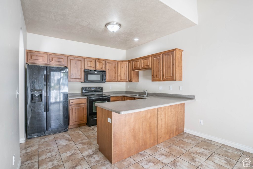 Kitchen featuring a peninsula, brown cabinets, a sink, black appliances, and light countertops