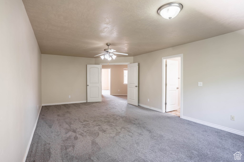 Carpeted empty room with a ceiling fan, baseboards, and a textured ceiling