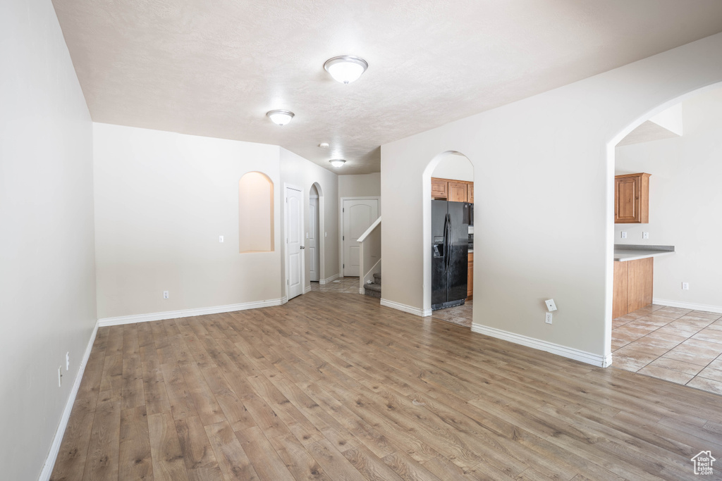Unfurnished living room featuring arched walkways, stairs, baseboards, and light wood-type flooring