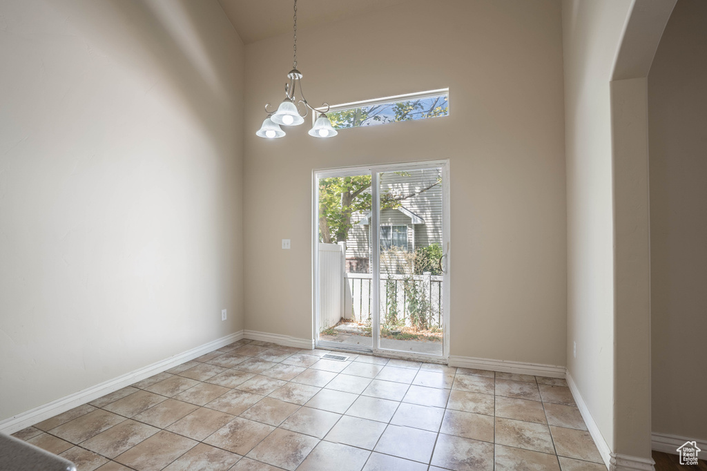 Unfurnished dining area featuring an inviting chandelier, a towering ceiling, arched walkways, and baseboards
