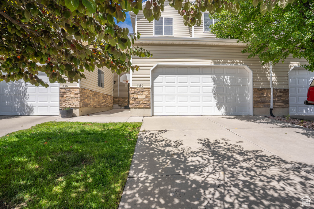 View of front facade featuring an attached garage, stone siding, and driveway