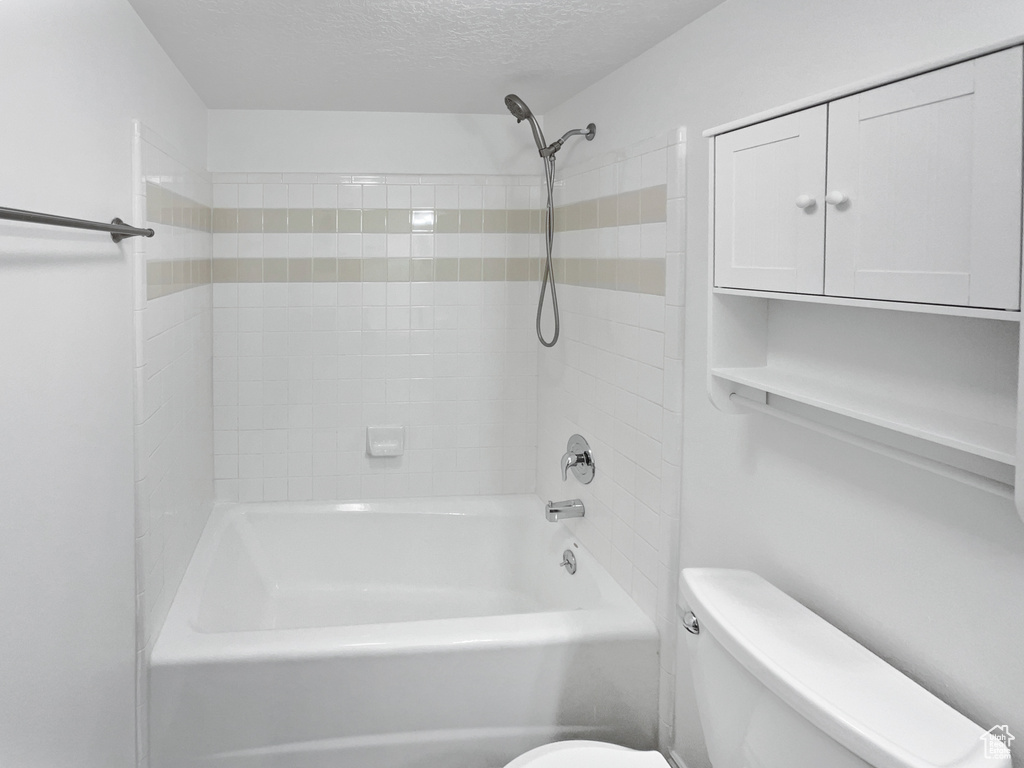 Bathroom with a textured ceiling, tub / shower combination, and toilet