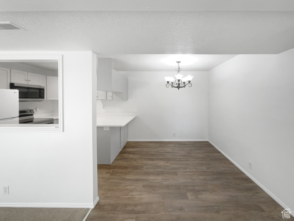 Unfurnished dining area featuring a textured ceiling, a chandelier, dark wood-style flooring, and baseboards