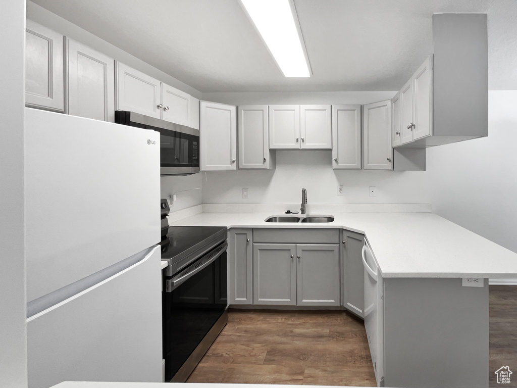 Kitchen featuring a sink, gray cabinets, light countertops, appliances with stainless steel finishes, and dark wood-style floors