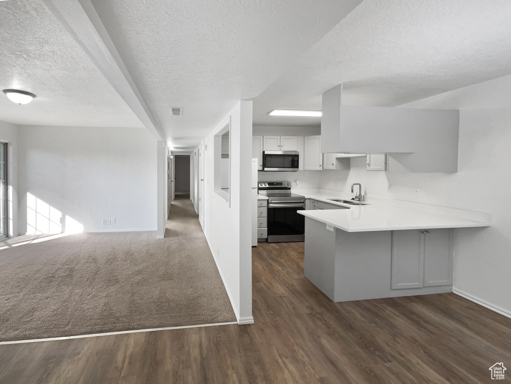 Kitchen featuring a textured ceiling, baseboards, a peninsula, open floor plan, and appliances with stainless steel finishes