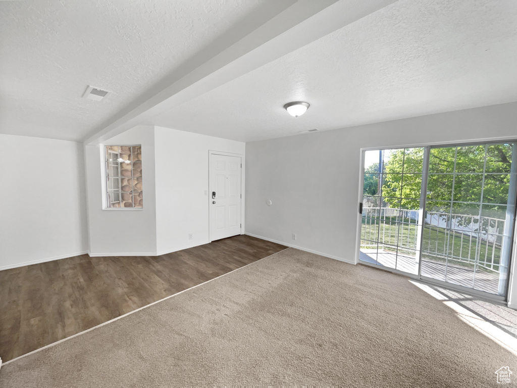 Unfurnished living room featuring baseboards, carpet, a textured ceiling, and wood finished floors
