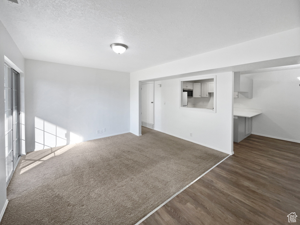 Unfurnished living room with dark wood finished floors, baseboards, and a textured ceiling