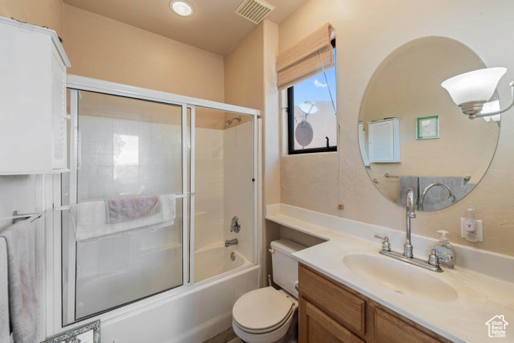 Bathroom featuring toilet, visible vents, vanity, and combined bath / shower with glass door