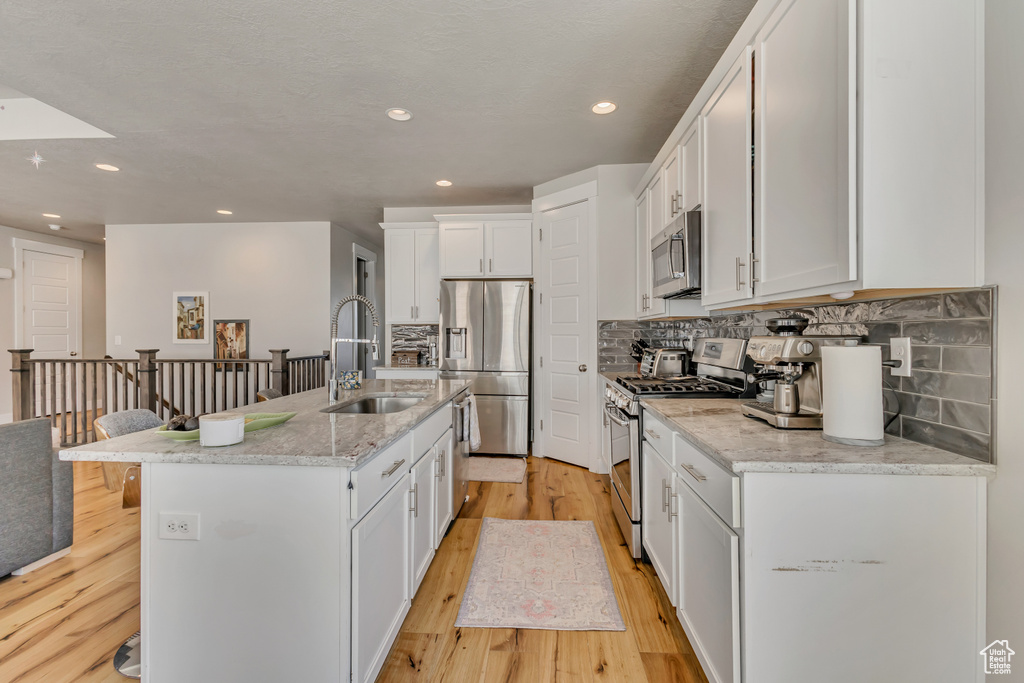Kitchen featuring a sink, stainless steel appliances, light wood finished floors, backsplash, and white cabinets