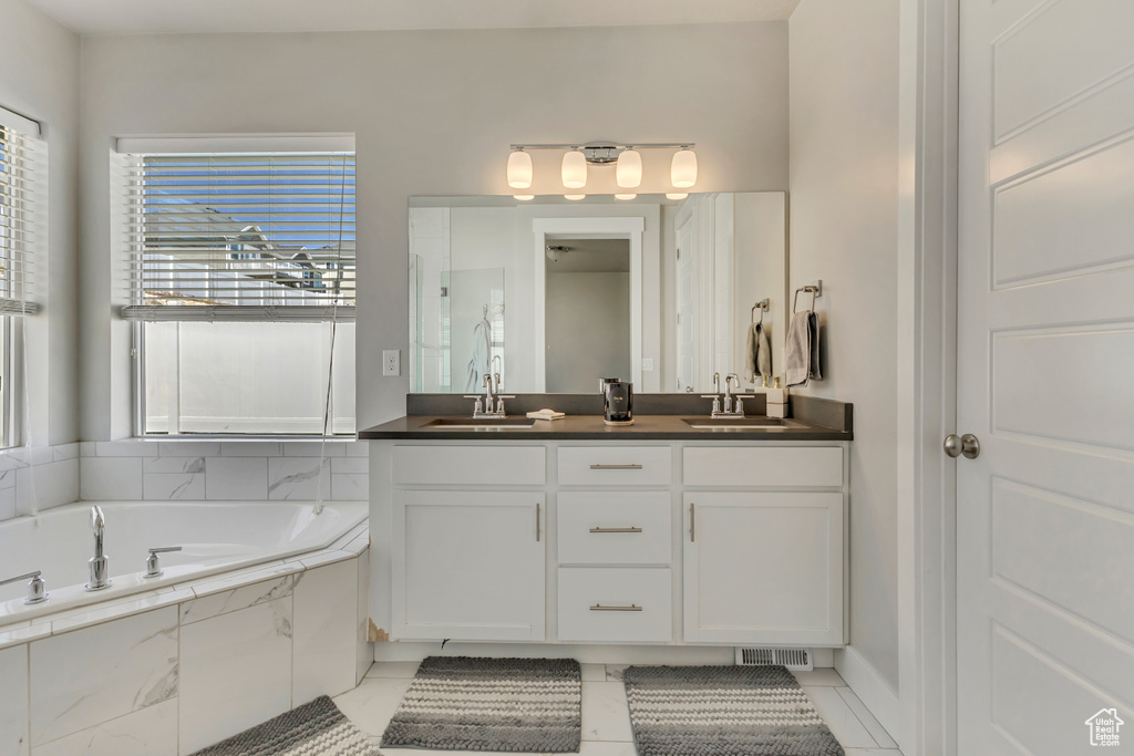 Full bath with tile patterned floors, double vanity, a bath, and a sink