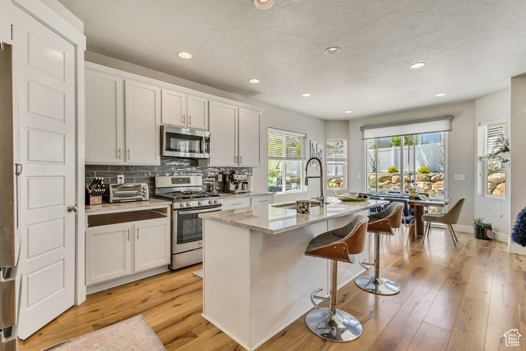 Kitchen featuring a sink, tasteful backsplash, an island with sink, a kitchen bar, and appliances with stainless steel finishes