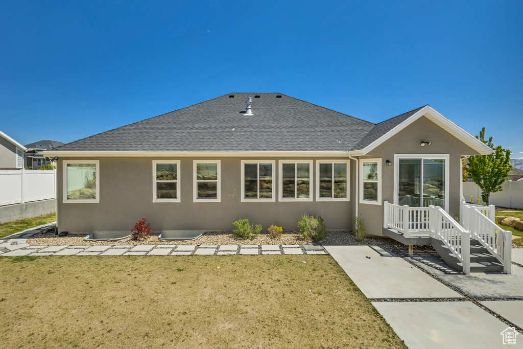 Back of house featuring a yard, stucco siding, roof with shingles, and fence