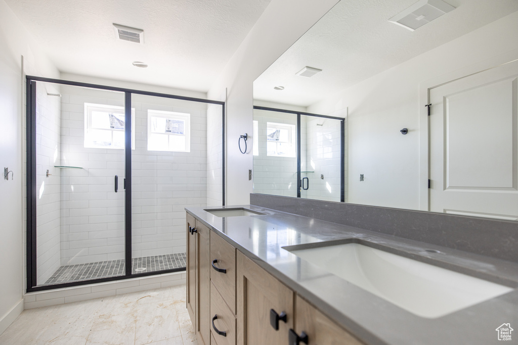 Bathroom featuring double vanity, visible vents, a stall shower, and a sink