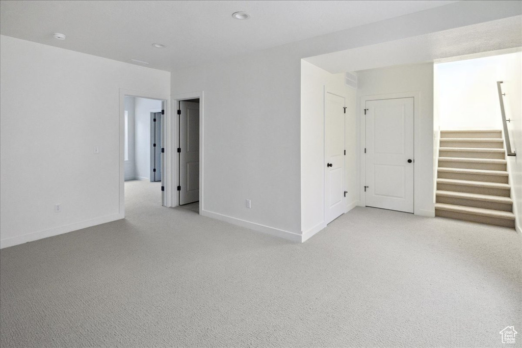 Spare room featuring light colored carpet, baseboards, stairway, and recessed lighting