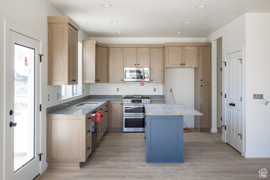 Kitchen with light brown cabinetry, light wood-style flooring, recessed lighting, a center island, and appliances with stainless steel finishes