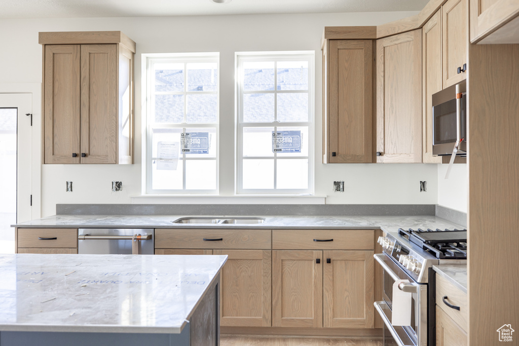 Kitchen featuring light stone countertops, stainless steel appliances, a sink, and light brown cabinetry