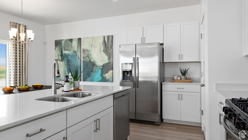 Kitchen with a sink, light wood-style floors, white cabinetry, light countertops, and appliances with stainless steel finishes