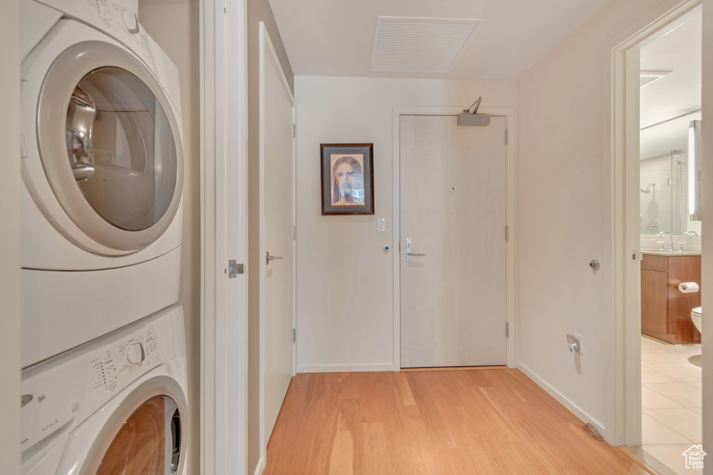Clothes washing area with light wood-style flooring, baseboards, a sink, laundry area, and stacked washer / drying machine