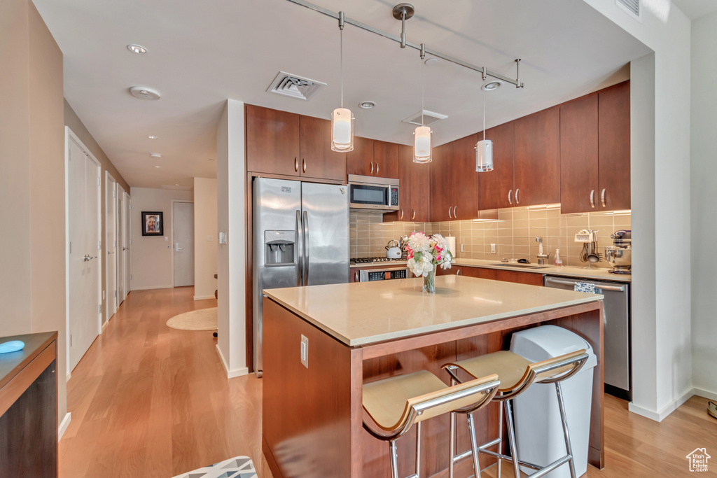 Kitchen featuring stainless steel appliances, visible vents, light wood finished floors, backsplash, and a center island