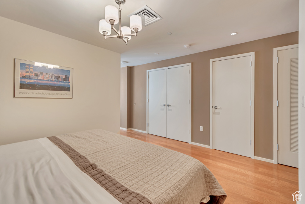 Bedroom with light wood-style flooring, two closets, visible vents, baseboards, and a chandelier