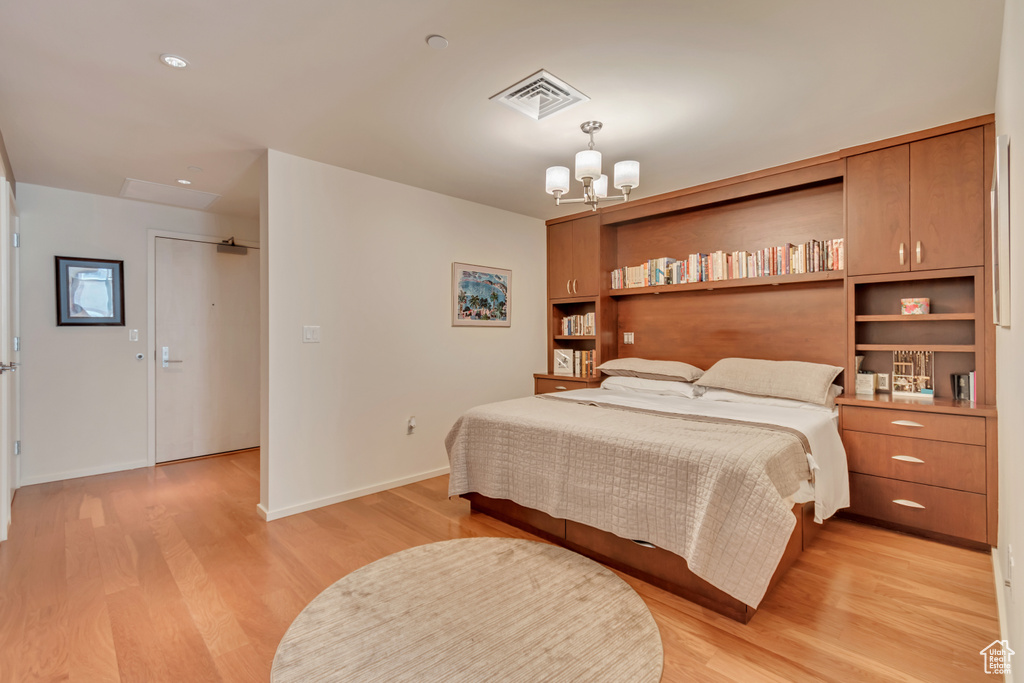 Bedroom with light wood finished floors, baseboards, visible vents, and an inviting chandelier
