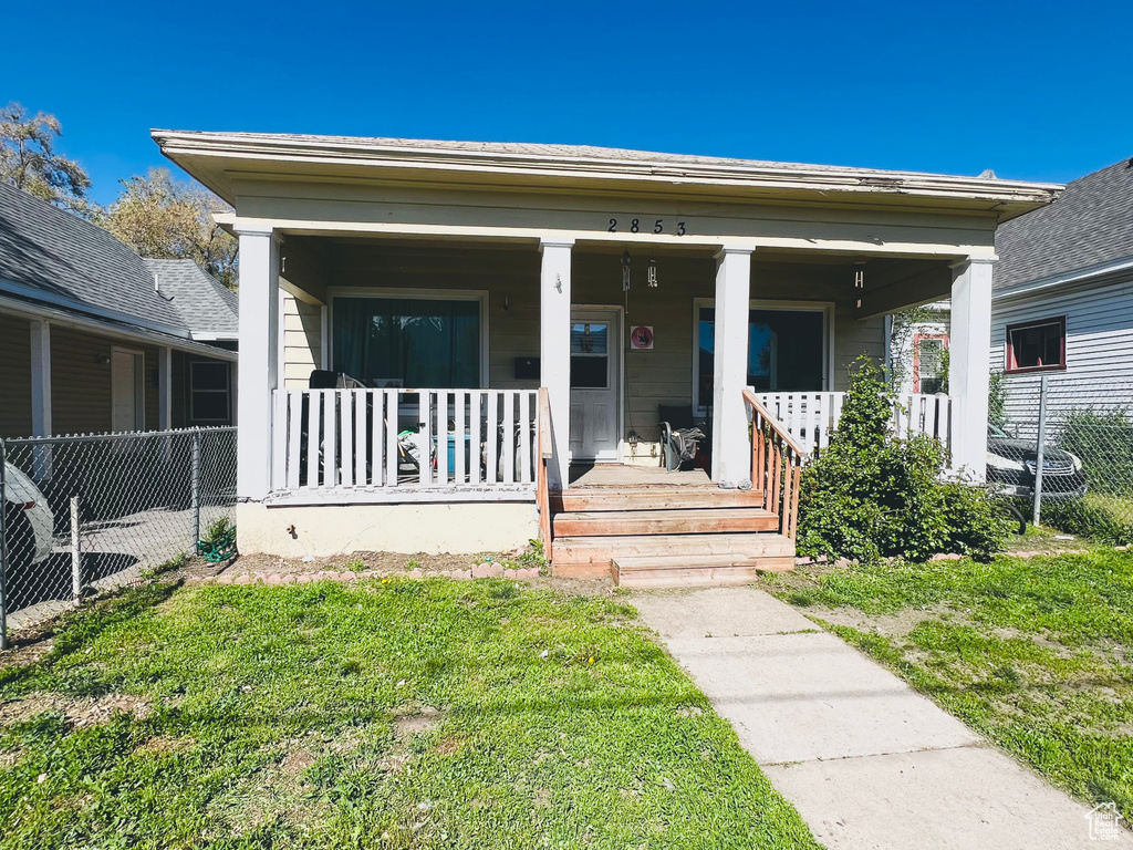 View of front of home featuring covered porch, fence, and a front yard