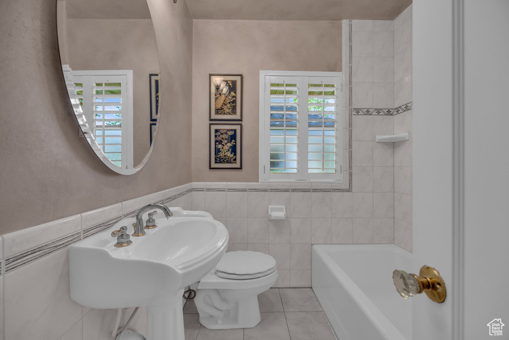 Full bath with a tub, toilet, tile patterned flooring, tile walls, and a wainscoted wall