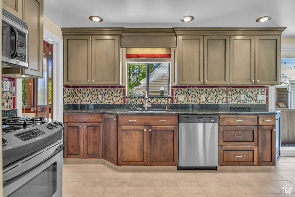 Kitchen featuring appliances with stainless steel finishes, backsplash, a sink, and dark stone counters