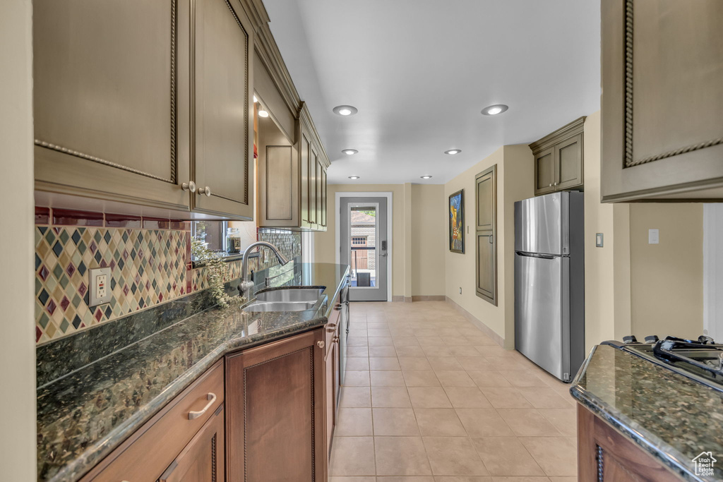 Kitchen with freestanding refrigerator, a sink, backsplash, light tile patterned flooring, and baseboards