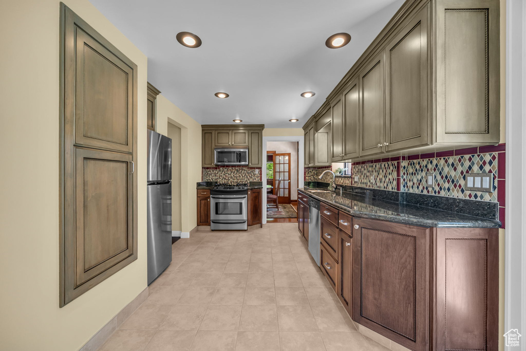 Kitchen featuring stainless steel appliances, a sink, backsplash, recessed lighting, and dark stone countertops