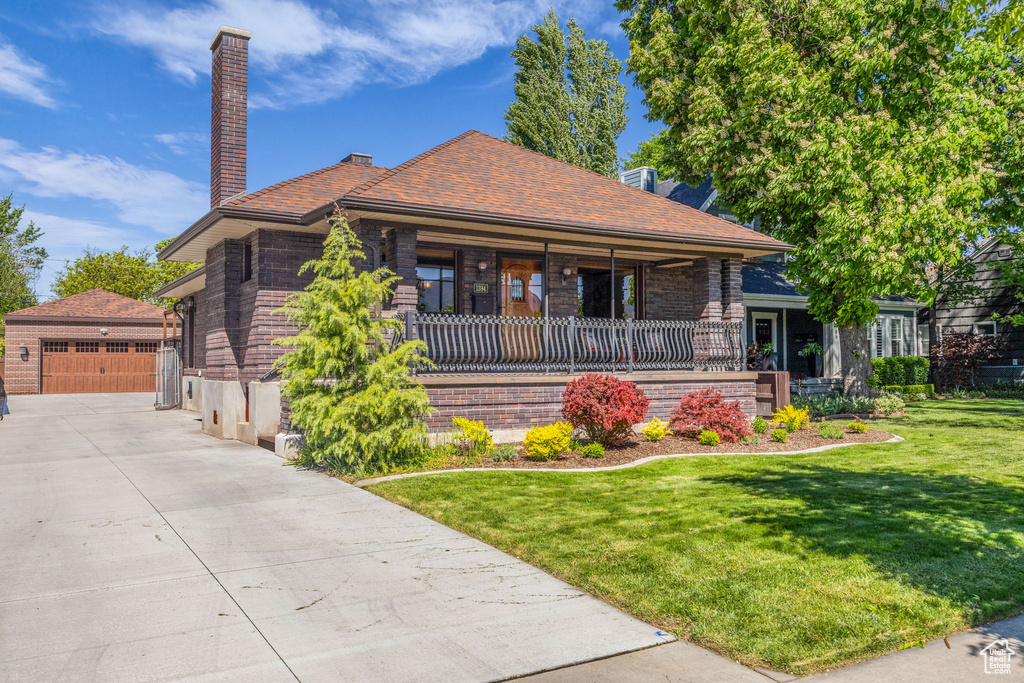 View of front of property with covered porch, a chimney, a front yard, an outdoor structure, and a garage