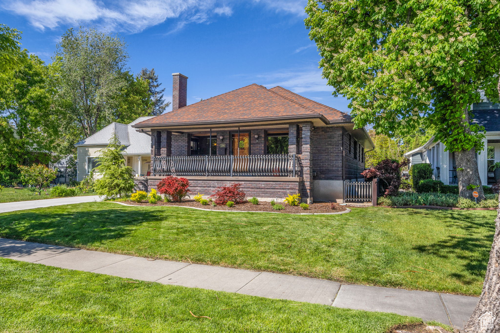 View of front of house with a chimney, brick siding, a front yard, and a porch