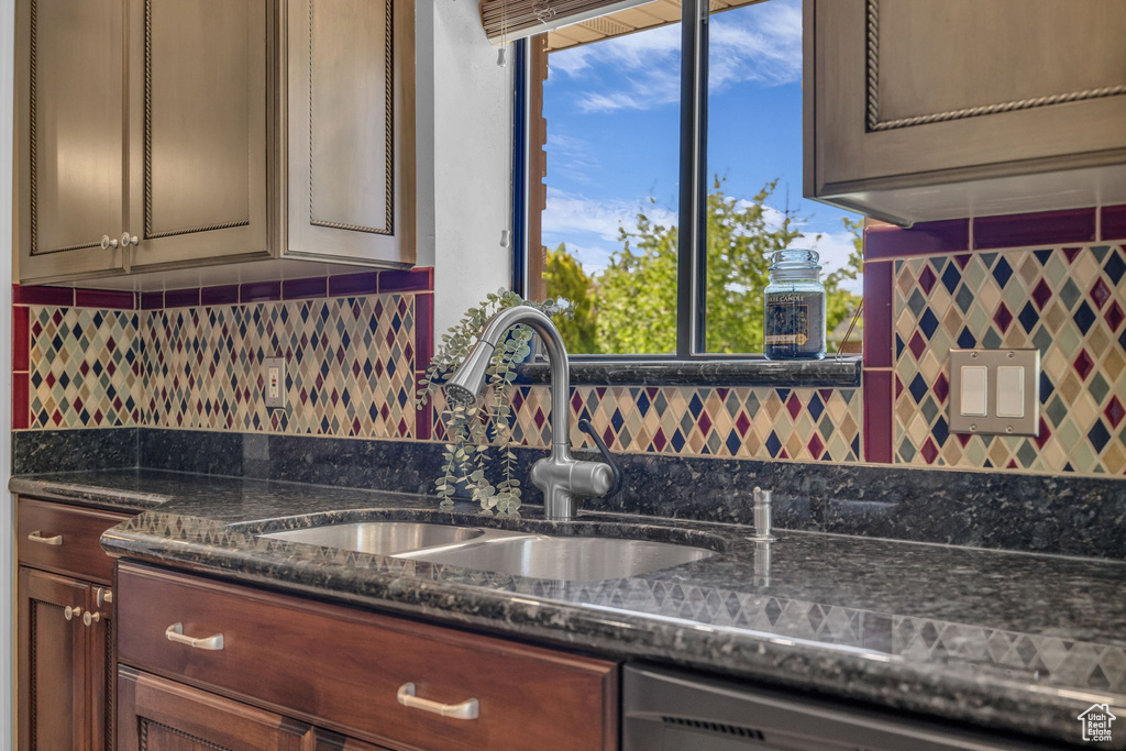 Kitchen featuring a sink, dishwashing machine, tasteful backsplash, and dark stone counters